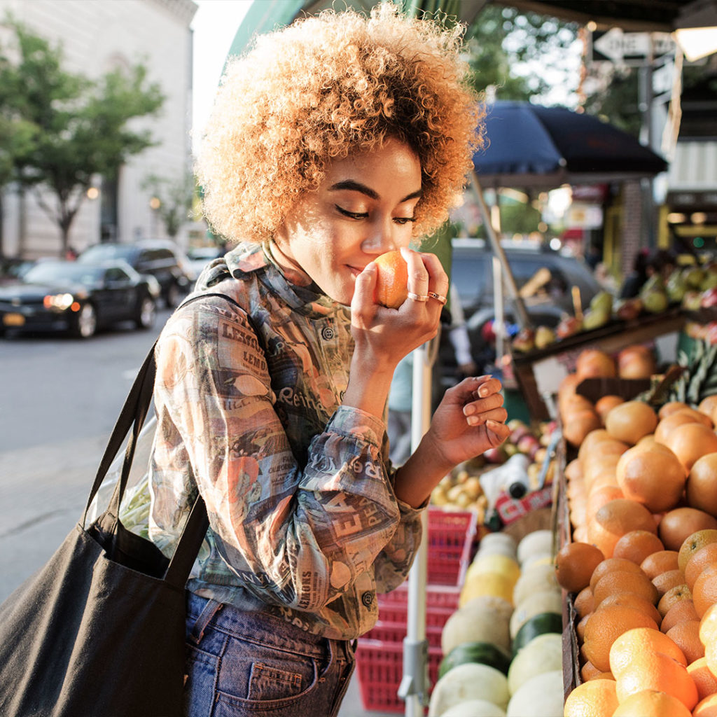 a woman sniffs an orange at the market